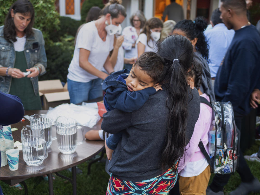 A woman, who is part of a group of migrants that had just arrived, holds a child as they are fed outside St. Andrews Episcopal Church on Wednesday in Edgartown, Mass., on Martha's Vineyard. Florida Gov. Ron DeSantis flew two planes of migrants to Martha's Vineyard on Wednesday.