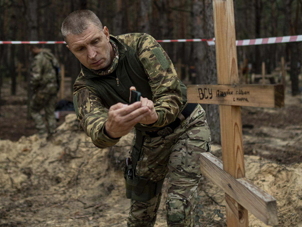 Oleg Kotenko, the commissioner for issues of missing persons under special circumstances, uses his smartphone to film the grave a Ukrainian soldier in the recently retaken area of Izium, Ukraine, Sept. 15, 2022.