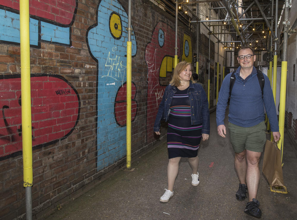 Charlotte Urwin and James Waller walk next to wall art at the Peckham Festival in London.