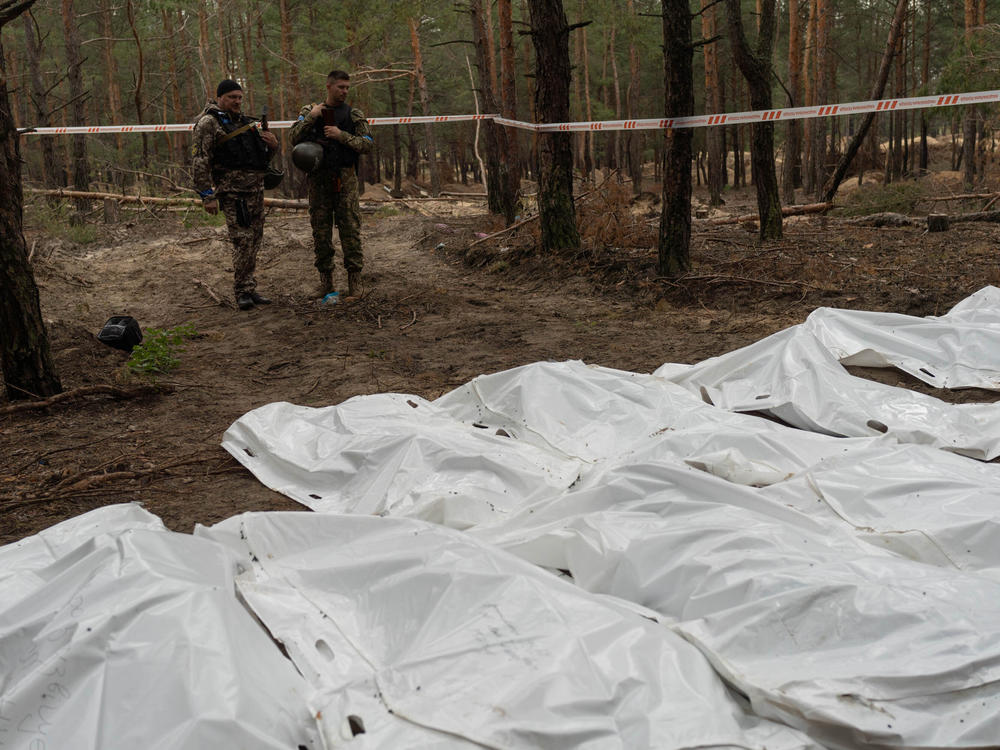 Ukrainian soldiers stand over bags containing the remains of exhumed bodies at a mass grave site in Izium, Ukraine.