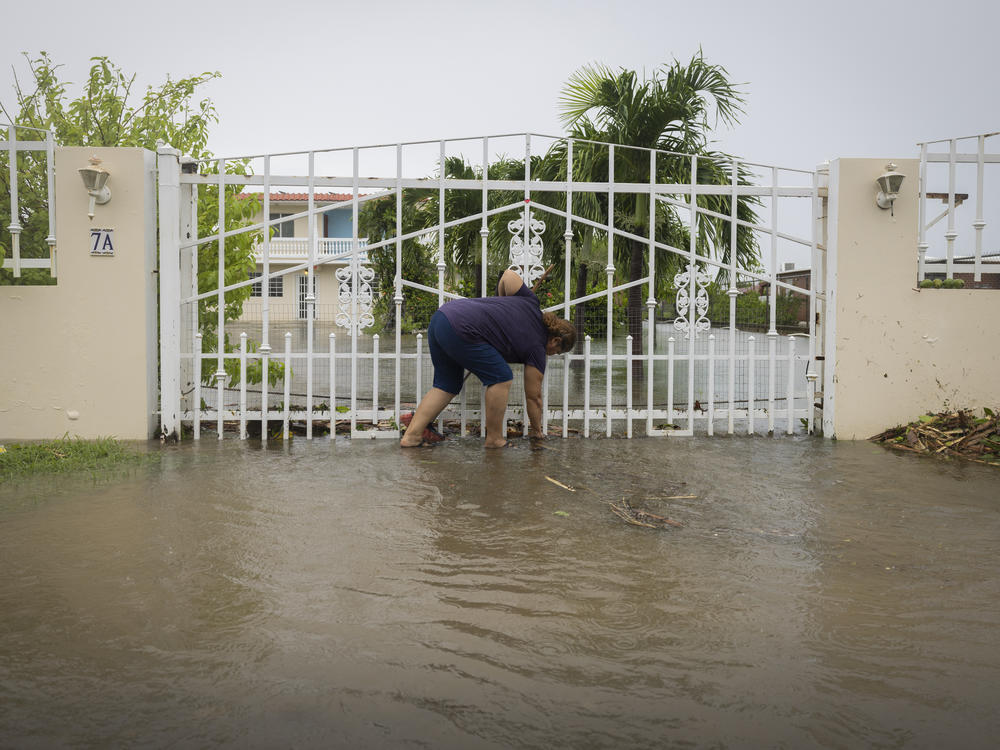 A woman clears debris on her property flooded by Hurricane Fiona in Salinas, Puerto Rico, Monday, Sept. 19, 2022.