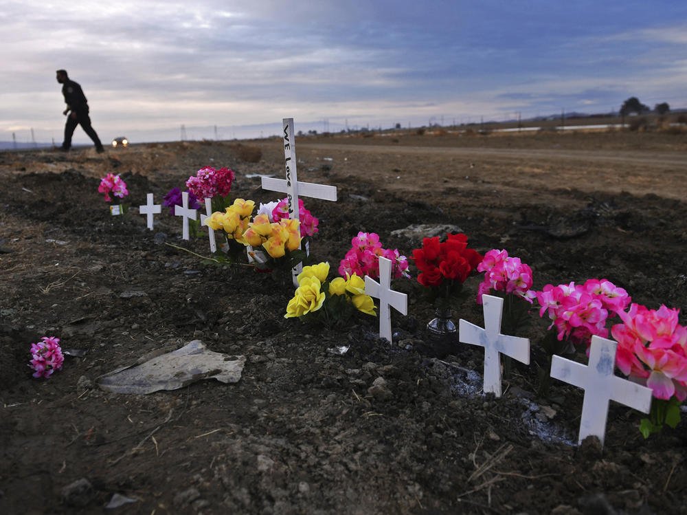 A row of crosses form a memorial along Highway 33 as police officers survey the scene a day after a crash killed nine people south of Coalinga, Calif., on Jan. 2, 2021.