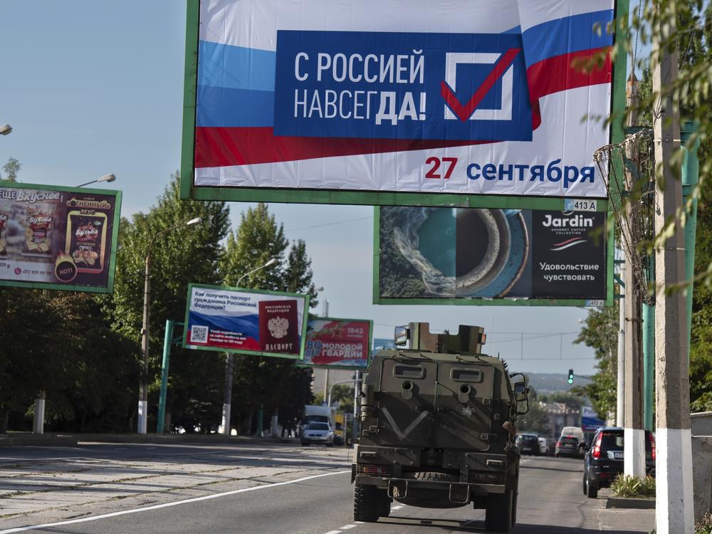 A military vehicle drives along a street in Russian-occupied Luhansk under a billboard that reads: 