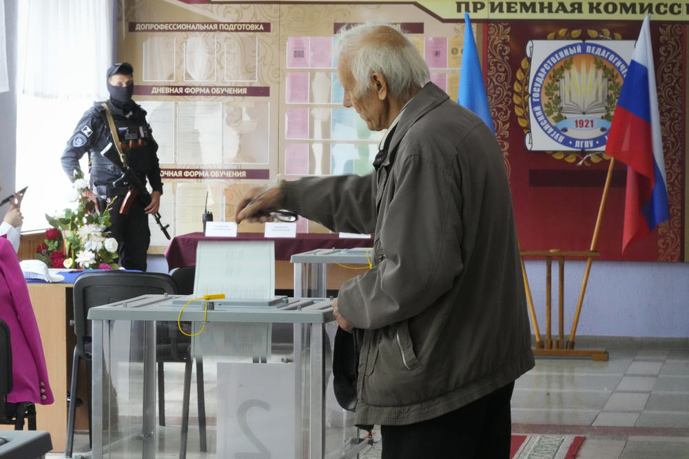 A man casts his ballot as a Russian soldier looks on in Luhansk, Ukraine, on Tuesday. Voting began Friday in four Moscow-held regions of Ukraine on referendums to become part of Russia.