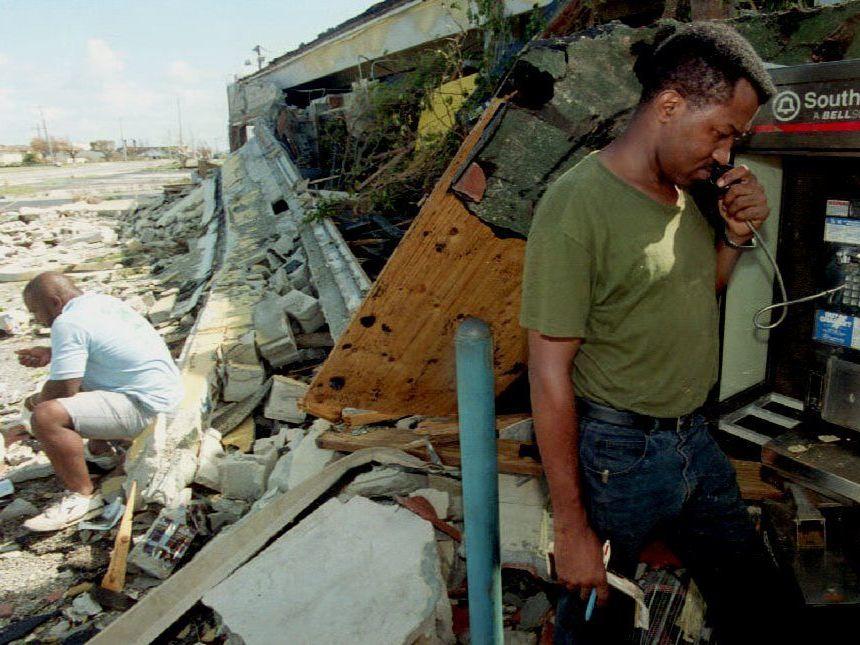A South Miami, Fla., resident makes a phone call from one of the few working phones in the area as another man waits for his turn amid the rubble of a destroyed business on Aug. 25, 1992, after Hurricane Andrew made landfall.