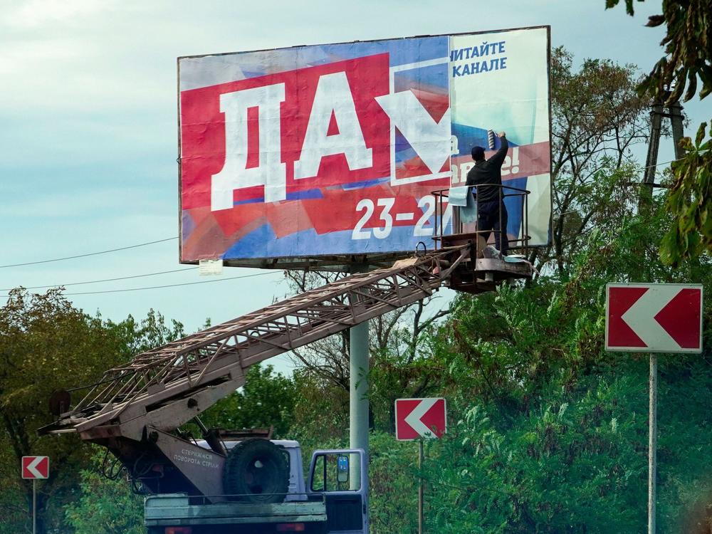 A man glues a referendum poster reading 