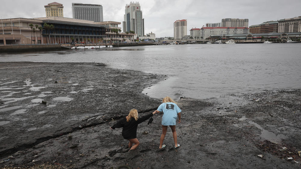 Sisters Angel Disbrow (right) and Selena Disbrow walk in the mud of a receded Tampa Bay on Wednesday as water was pulled out in advance of Hurricane Ian's arrival.