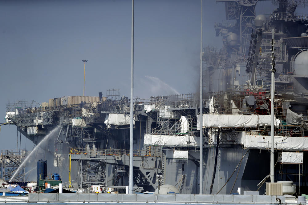 Fire crews spray water from the dock onto the side of the USS Bonhomme Richard, in San Diego, July 12, 2020.