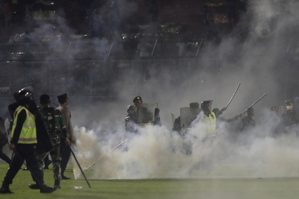 Police officers and soldiers stand amid tear gas smoke during a soccer match at Kanjuruhan Stadium in Malang, East Java, Indonesia, on Saturday. Clashes between supporters of two rival teams broke out after the match. More than 100 were killed.