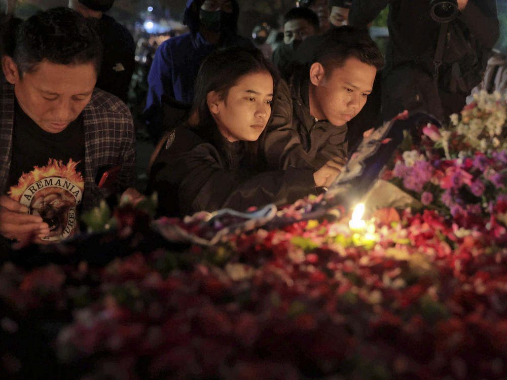 People lay flowers during a candle light vigil for the victims of Saturday's soccer riots outside Kanjuruhan Stadium where it broke out, in Malang, East Java, Indonesia, Sunday, Oct. 2, 2022.