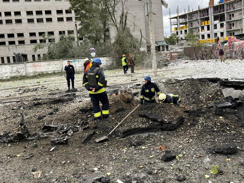 Emergency workers clear debris from the crater of a missile strike at a bus stop in a residential area of Dnipro, Ukraine. Missiles struck multiple cities across the country Monday morning.