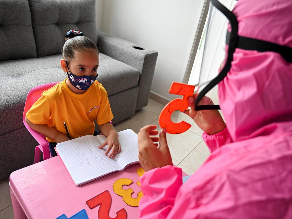 Giving a lesson at the home of a girl in Cali, Colombia, in August 2020, a teacher wears a biosecurity suit to prevent infection from the novel coronavirus. The 