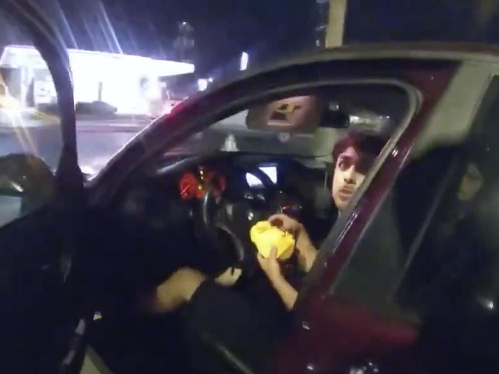 In this image taken from Sunday, Oct. 2, 2022, police body camera video and released by the San Antonio Police Department, Erik Cantu looks toward San Antonio Police Officer James Brennand while holding a hamburger in a fast food restaurant parking lot.