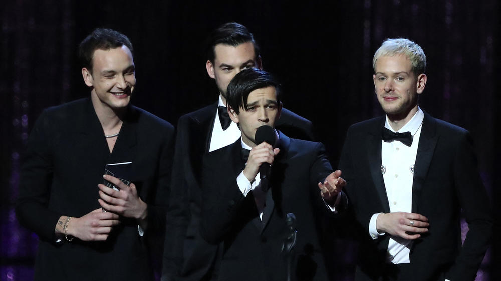 Healy (with microphone) and the other members of The 1975 (from left: George Daniel, Ross MacDonald and Adam Hann) accept the award for British Album of the Year at the 2019 BRIT Awards.
