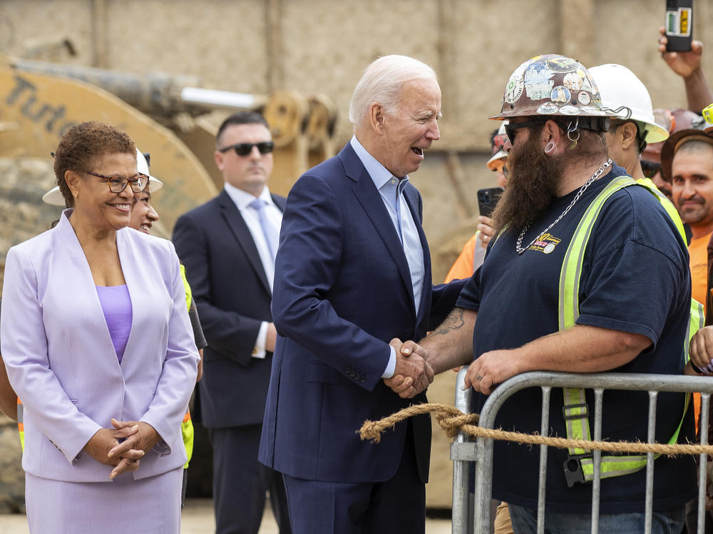 President Biden greets Kevin Corbin, a heavy equipment operator at a Los Angeles metro construction project, as Rep. Karen Bass — who is running for LA mayor — looks on.