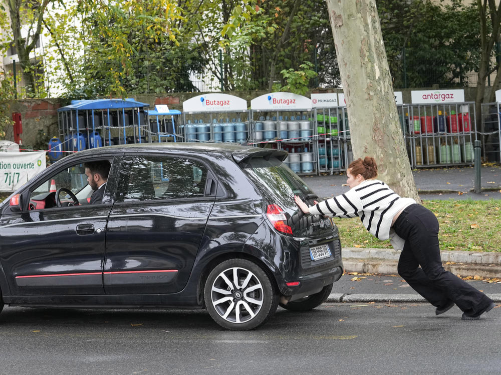 A woman pushes her car to reach a gas station on Oct. 14, 2022 in Nanterre, outside Paris. Strikes in the French refineries of TotalEnergies group continued Friday, heavily disrupting fuel supplies.