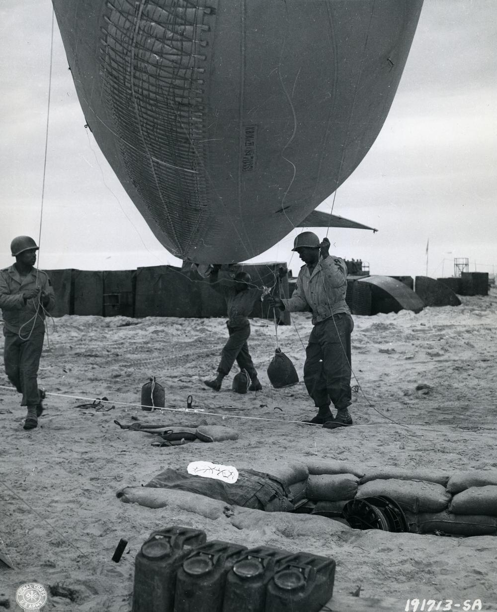 Cpl. A. Johnson, from Houston, is assisted by some of his men as they walk a balloon over to a winch, in France on July 24, 1944.