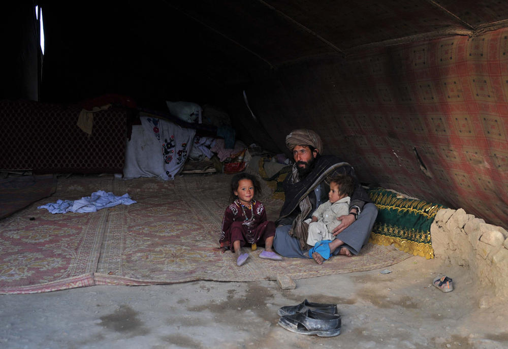 An Afghan internal refugee man sits in a tent with two children on the outskirts of Jalalabad.