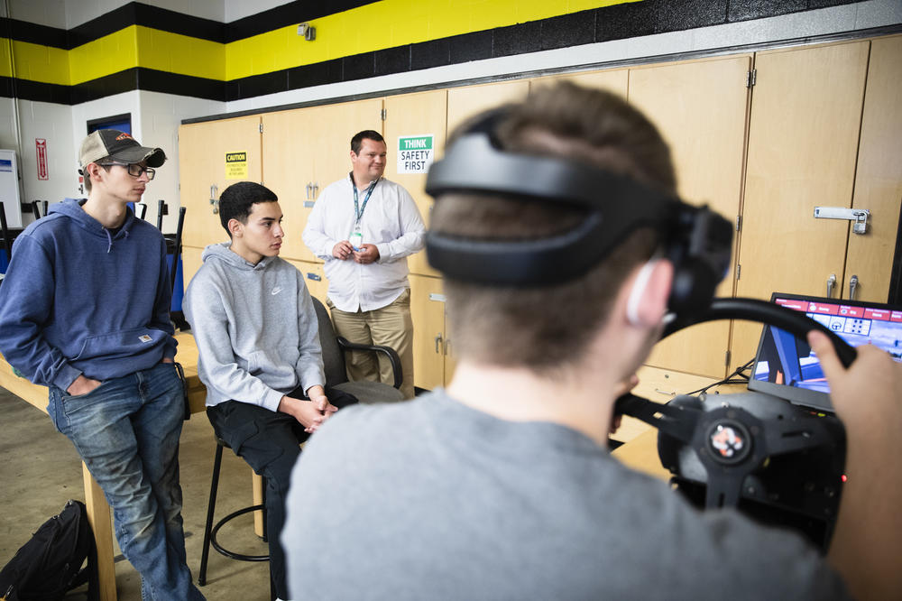 Tucker Bubacz, Peter Vilas Novas, and instructor Eric Young look on as Joshua Hewitt practices navigating intersections on a simulator, a big component of their training before they get their permits.