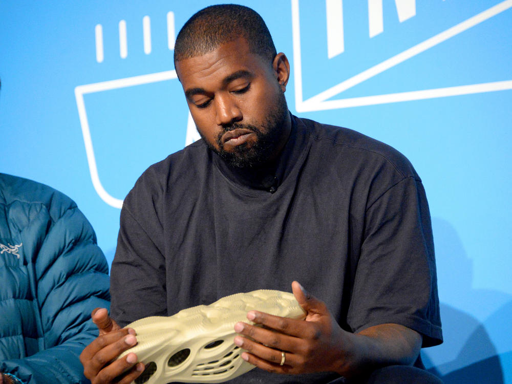 Kanye West holds a Yeezy shoe as he speaks on stage at the 