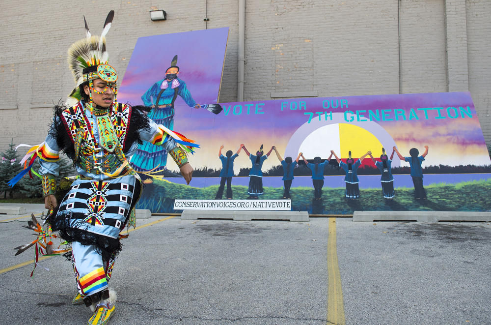 Damian Funmaker performs a traditional Ho-Chunk dance with the Wisconsin Dells Singers and Dancers during an event hosted by Wisconsin Native Vote to encourage voting at the Gerald L. Ignace Indian Health Center in Milwaukee, on Friday. The mural in the background, painted by Christopher Sweet, and reads, 
