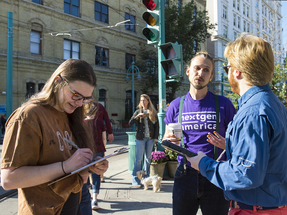 Matthew Grover (center) of NextGen America talks with young voters Kate Browning (left) and Jack Borg as they sign a pledge promising to vote near the Milwaukee Public Market on Saturday.