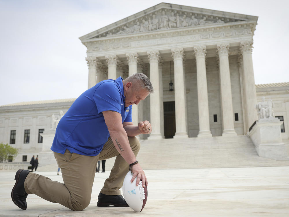 Joseph Kennedy, seen here taking a knee in front of the U.S. Supreme Court last spring, will return to coach at Bremerton High School. His practice of praying on the field sparked a court case over accommodating religious expression in public schools.
