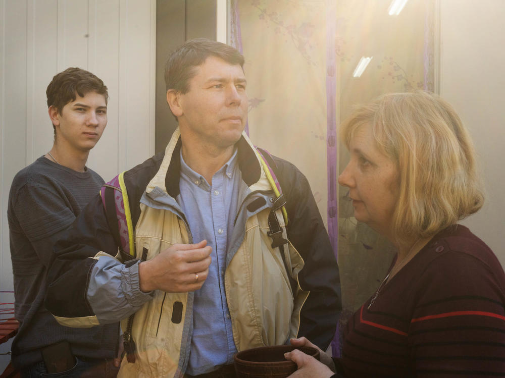 Volodymyr Korchevsky (center) stands with his son Bohdan, 18, and wife, Hanna Korchevska, outside their temporary home in Lviv. The Korchevsky family left the middle-class life they'd built in Mariupol and now months later, jobs gone, savings depleted and unable to afford rent, they are living in what's essentially a short shipping container, sandwiched between others, in a Lviv city park.