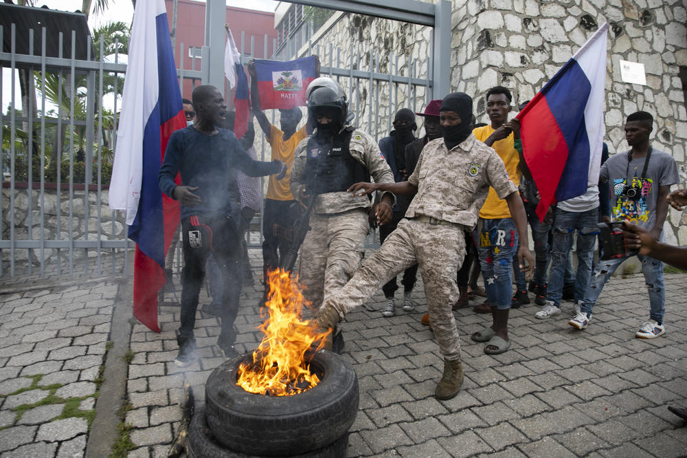 A police officer kicks a burning tire, set on fire by protestors, in front of the Canadian Embassy during a protest against the government's request for an international military force in Port-au-Prince on Oct. 24.