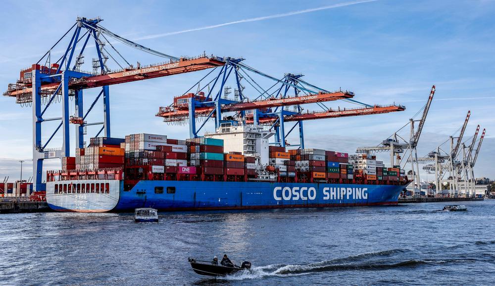 Small boats pass in front of  a COSCO Shipping Corporation container ship as it is unloaded at the Port of Hamburg on Oct. 26.
