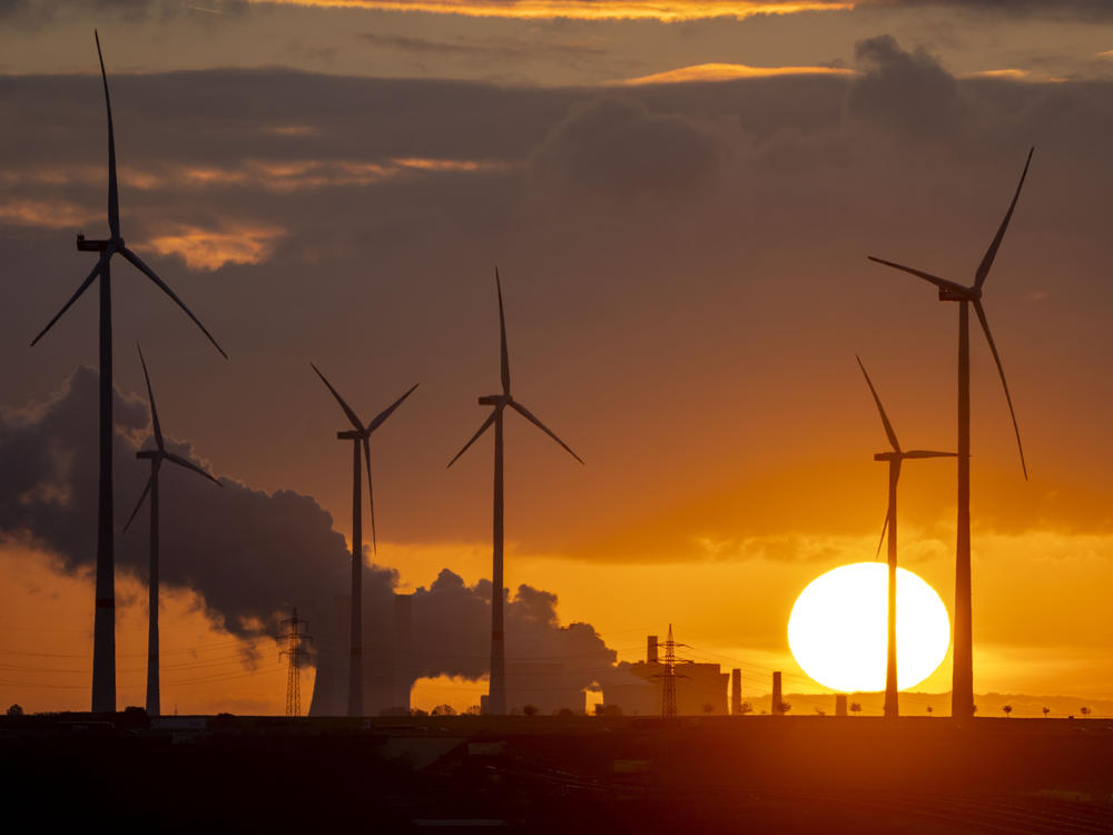 Steam rises from the coal-fired power plant with wind turbines nearby in Niederaussem, Germany, as the sun rises on Nov. 2, 2022.