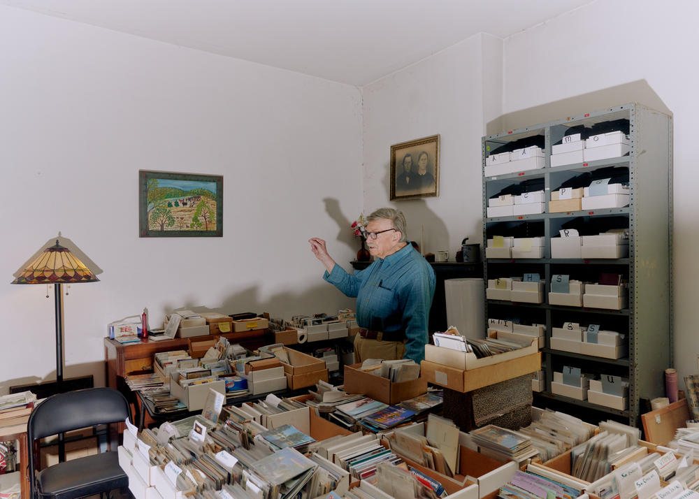 Brown poses for a portrait inside his home surrounded by some of his many postcards.