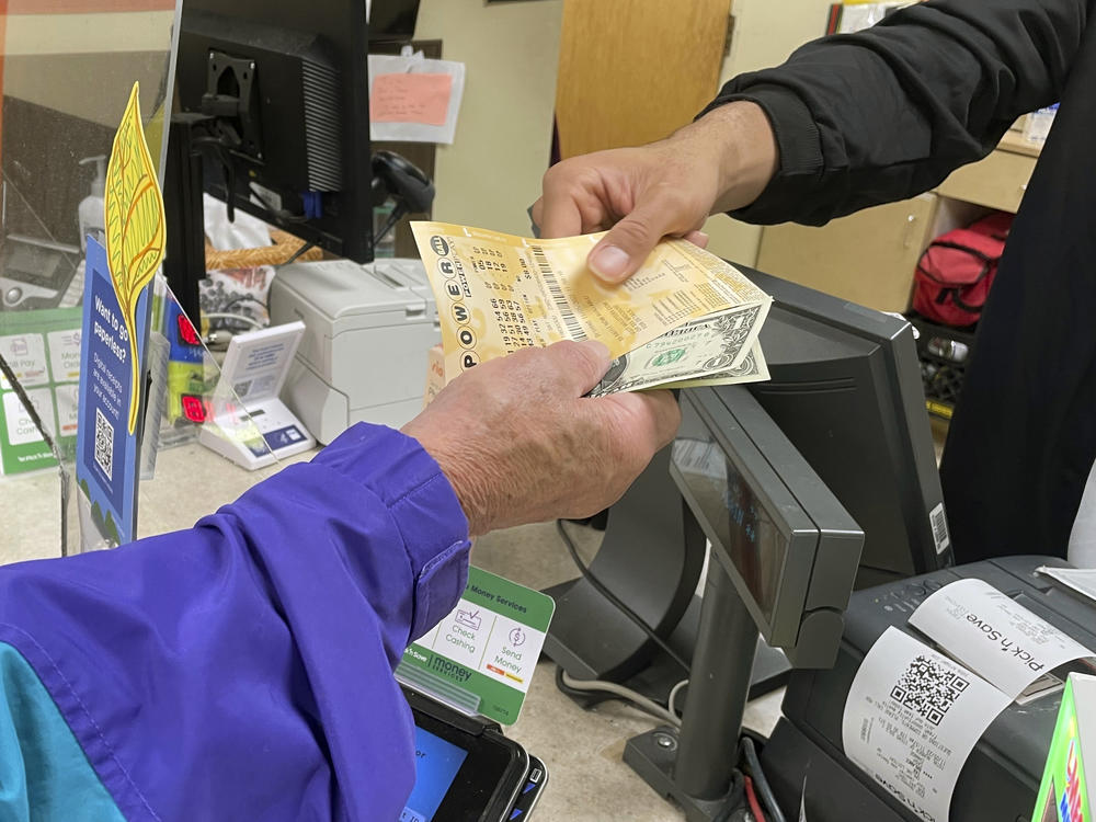From behind the lottery counter at a Pick 'n Save store in Madison, Wis., Djuan Davis hands Powerball tickets to Arpad Jakab, a retired utility worker who said it's his first time buying them.