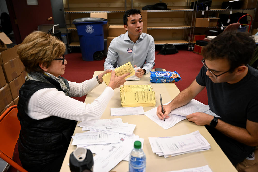 Poll workers open and verify that absentee ballots were signed and placed in their envelopes correctly by processed by a tabulation machine in New Haven's hall of records on Nov. 8, 2022.