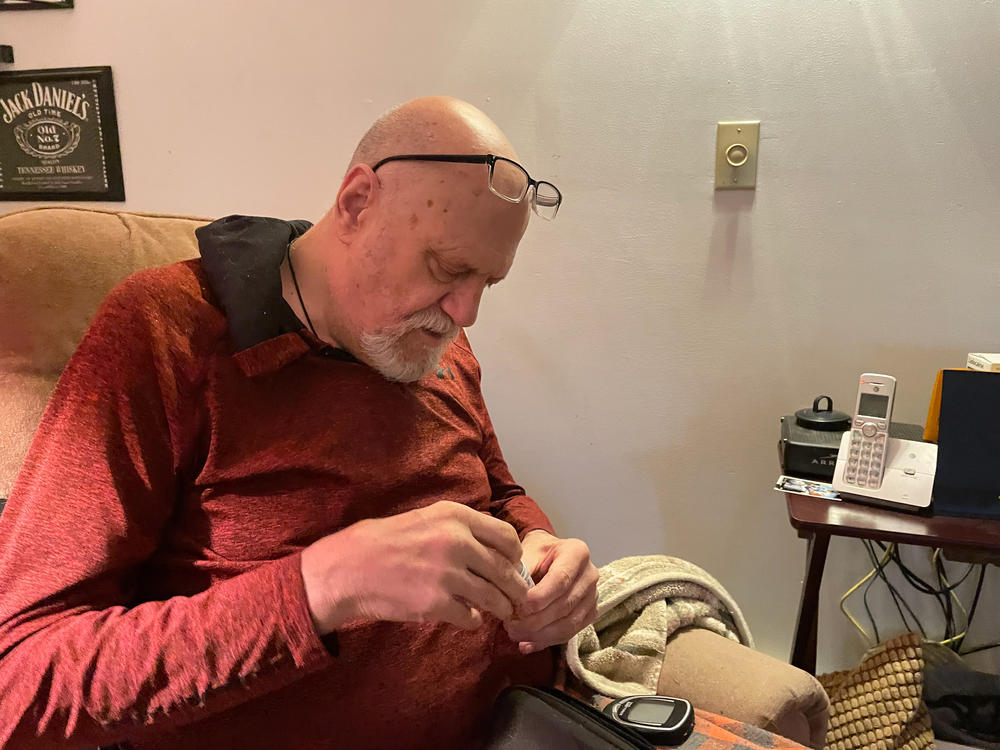 Kim Hilton, who has Type 2 diabetes, checks his blood sugar while friends sort through his belongings on the day he moved out of his house because of a rent hike.