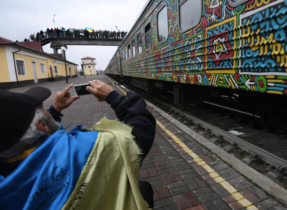 A man photographs the train and people line the bridge above as the train arrives in Kherson on Saturday. Some of the train cars had been decorated by Ukrainian artists.