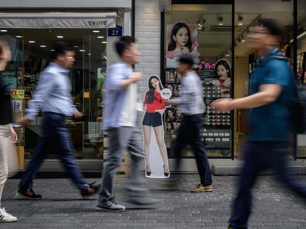 Shoppers walks past cosmetic stores in the Myeongdong district of Seoul in 2019. Women in South Korea are held to a beauty standard many believe to be unfair and inappropriate.