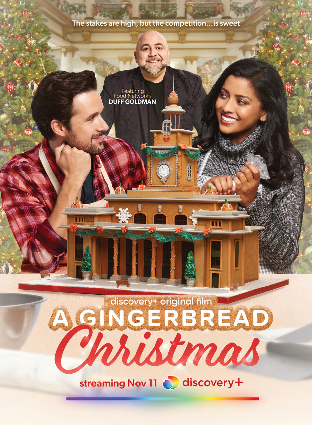 The promotional art for <em>A Gingerbread Christmas</em> on Discovery+, in which Tiya Sircar and Marc Bendavid are watched over by the Ace of Cakes himself, Duff Goldman.