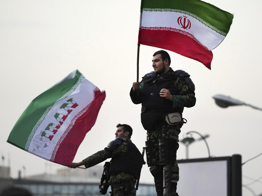 Two anti-riot police officers wave the Iranian flags during a street celebration after Iran defeated Wales in Qatar's World Cup, at Sadeghieh Sq. in Tehran, Iran, Friday, Nov. 25, 2022.