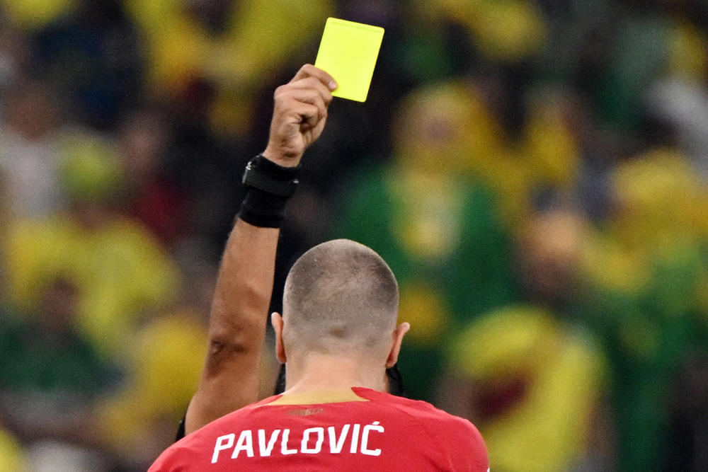 Iranian referee Alireza Faghani (back) holds up a yellow card for Serbian defender Strahinja Pavlovic (No. 2) during a 2022 World Cup Group G match between Brazil and Serbia on Thursday, Nov. 24, 2022, at the Lusail Stadium in Lusail, north of Doha, Qatar.