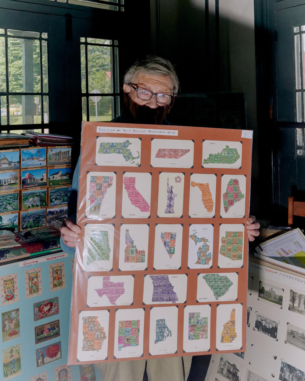 Brown holds up a board of old state postcards in his home in June.