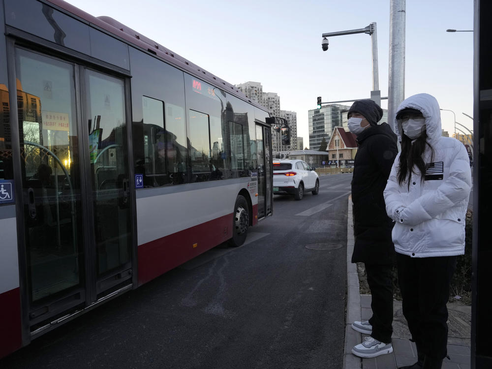 Residents wearing masks wait at a public bus stop in Beijing on Saturday. Chinese authorities announced a further easing of COVID-19 curbs with major cities such as Shenzhen and Beijing no longer requiring negative tests to take public transport.