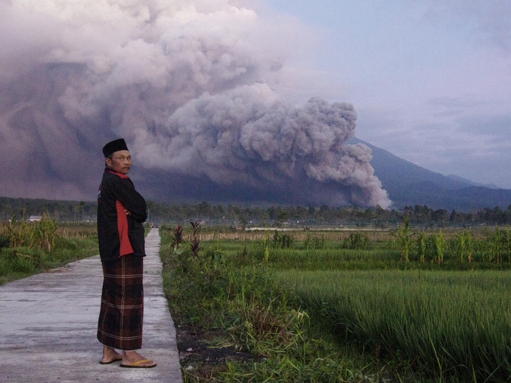 A man looks on as Mount Semeru releases volcanic materials during an eruption on Sunday, Dec. 4, 2022 in Lumajang, East java, Indonesia. Indonesia's highest volcano on the country's most densely populated island of Java erupted Sunday.