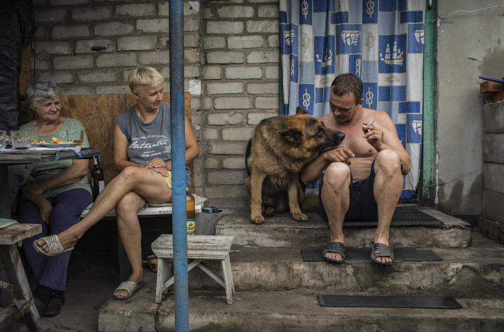 Elena Dyachkova (center) and Aleksander Dokalenko (right), and their dog, Lord, share a dinner with their neighbor, Valentina (left), at their house in Avdiivka in July 2018.