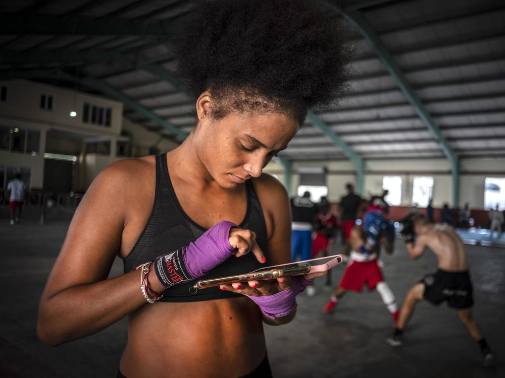 Boxer Giselle Bello Garcia texts on a mobile phone while other athletes train at a boxing gym in Havana, Cuba, Monday, Dec. 5, 2022.