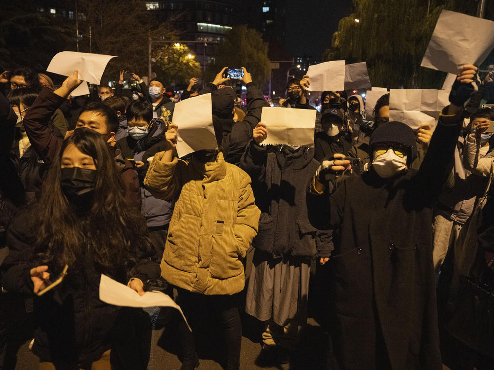 Protesters hold up blank papers and chant slogans as they march in protest in Beijing, Sunday, Nov. 27, 2022.