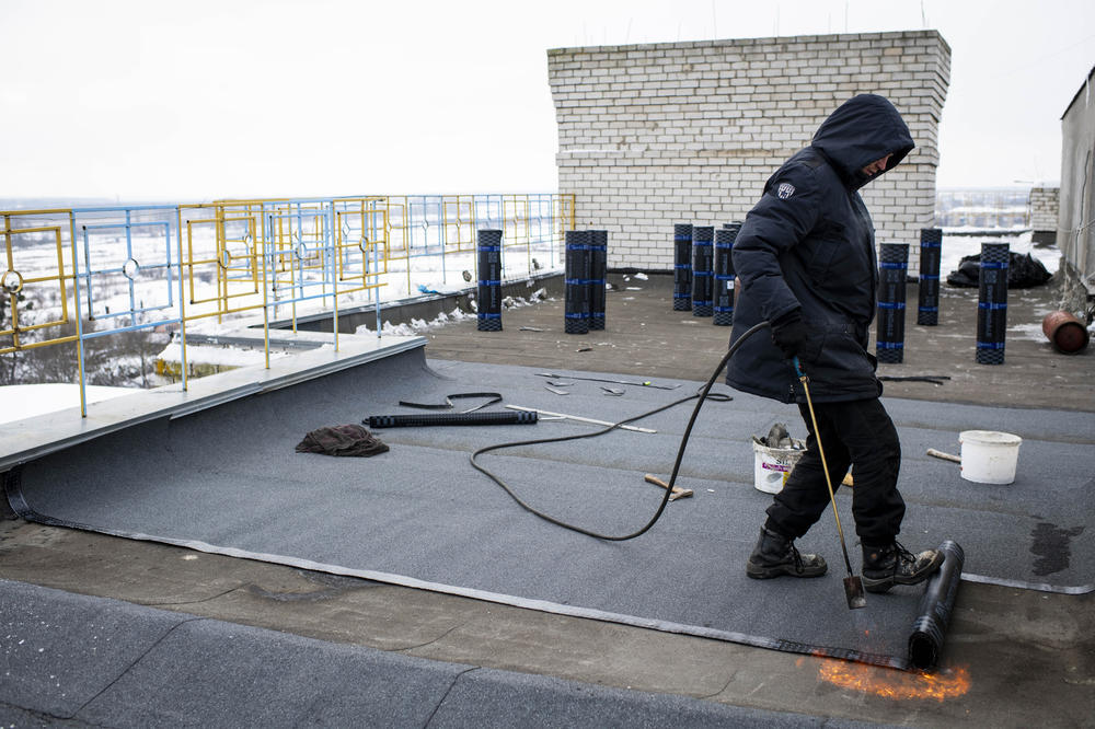 Artyom Haydanka works to repair the roof of a damaged apartment building on the main square in Borodianka on Monday.