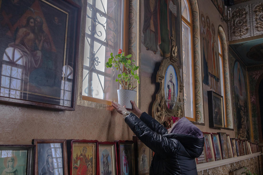 A woman places a plant on the windowsill at the Church of the Archangel Saint Michael after morning service in Borodianka on Sunday.