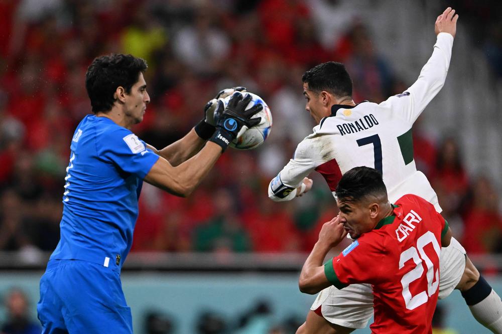 Morocco's goalkeeper Yassine Bounou, also known as Bono (left), saves a shot by Portugal's Cristiano Ronaldo (top) next to Morocco's defender Achraf Dari during a 2022 World Cup quarterfinal match on Saturday, Dec. 10, at the Al-Thumama Stadium in Doha, Qatar.