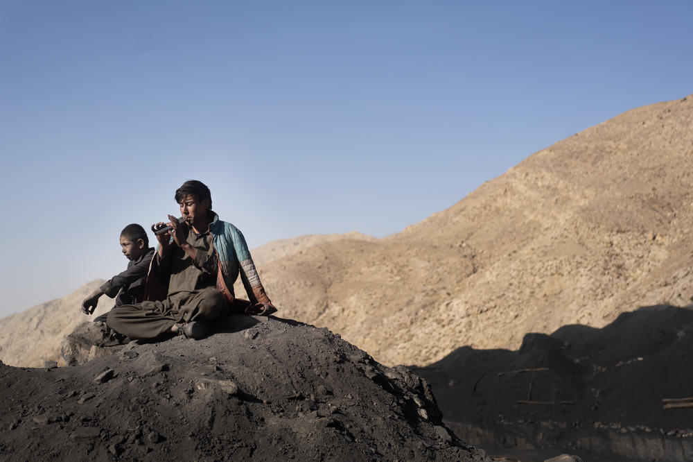 Boys sit on the mountain after a 10-hour work day and play the flute.